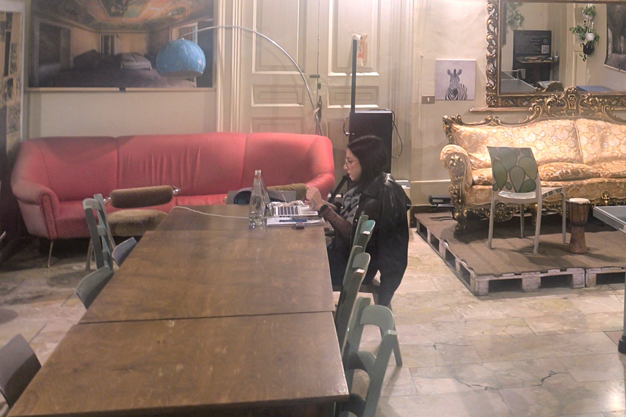 Coworking room at Ostello degli Elefanti with frescoed ceiling, vintage furniture and a guest working on a laptop.